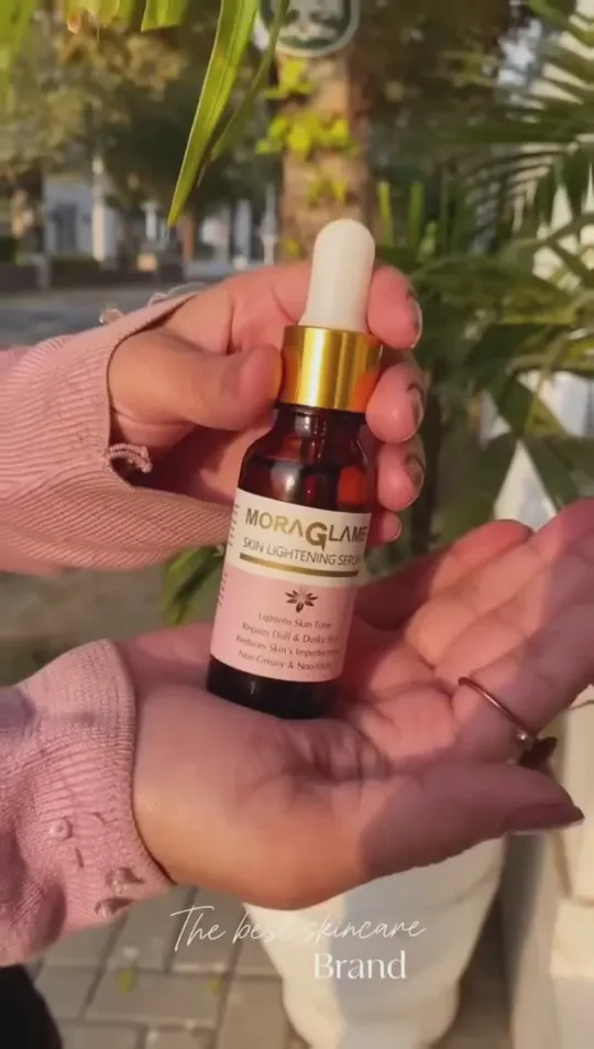 A hand holding MoraGlame Skin Lightening Serum outdoors